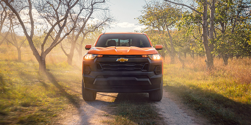Orange Chevrolet pickup truck driving on a Name: wooded area, highlighting its off-road capability and rugged performance.